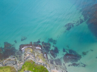 Aerial top-down view of turquoise sea waves crashing over rocky coastline with moss and clear water. Wild nature texture along the Bulgarian coast, dramatic and scenic