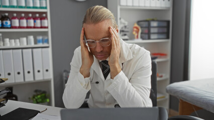 Doctor man in clinic stressed, wearing white coat with hands on head, surrounded by medical...
