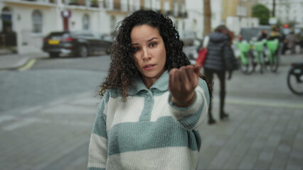Fototapeta premium Young hispanic woman gesturing outdoors on a street, with people and bicycles in the background, capturing an urban scene in a lively city setting.