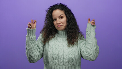 Hispanic woman in a green sweater making quotation marks with her fingers, standing against a purple background, expressing uncertainty or sarcasm.