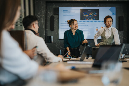A diverse group of business people engaged in a collaborative meeting. Charts and graphs displayed on a screen indicate data analysis and teamwork. The atmosphere is dynamic and interactive.