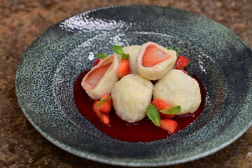 Fruit dumpling with strawberry sauce served on a blue plate – traditional sweet dish with vibrant colors and soft texture.