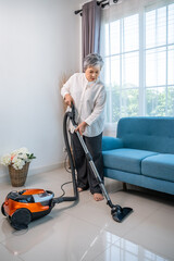 Senior elderly Asian woman vacuuming clean tiled floor at home