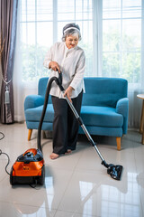 Senior Asian woman vacuuming floor while enjoying music with headphones at home