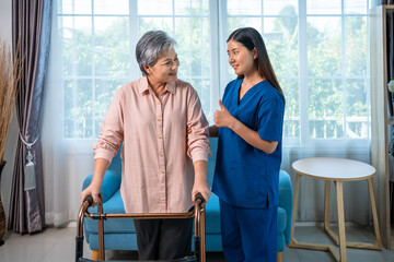Female caregiver supporting senior woman using walker with encouragement at home