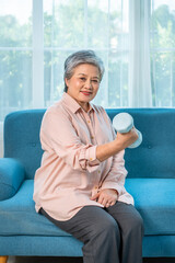 Elderly Asian woman lifting dumbbell at home for strength and healthy aging, looking at camera