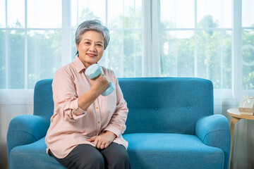 Senior Asian woman exercising with dumbbell at home for healthy aging and strength training, looking at camera