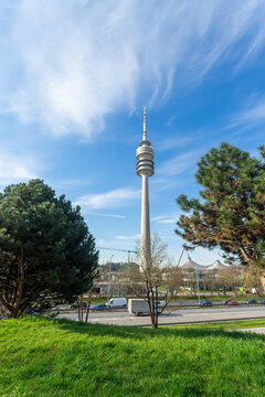 Munich, Bavaria, Germany - April 9 2025: The Olympic Tower stands tall under a bright blue sky, framed by trees and traffic near Olympiapark in springtime.