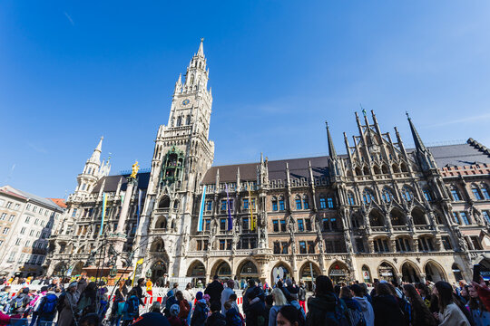 Munich, Bavaria, Germany - April 9 2025: Crowds gather at Marienplatz in front of the New Town Hall with its Gothic fa&ccedil;ade and famous Glockenspiel on a bright spring day.