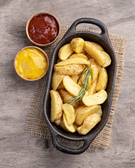 Rustic baked potatoes in a plate with ketchup, mustard and beer over wooden table