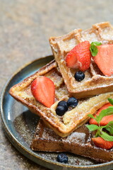 Bright and airy breakfast scene featuring waffles topped with fresh strawberries, blueberries, and mint leaves, beautifully plated.