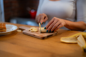 A close-up photo of hands cutting a banana on a wooden cutting board, with other ingredients nearby.