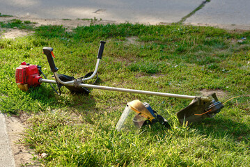 Lawn tool and protective mask lying on green yard space, ongoing mowing work and the combination of safety and efficiency in outdoor landscaping. Face cover and weed trimmer idle on grass patch