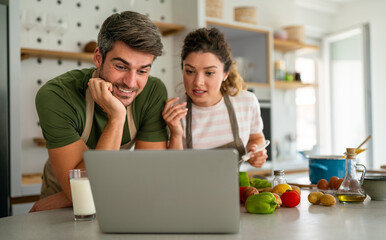 Young couple using laptop computer to take part in online culinary workshop, cooking together