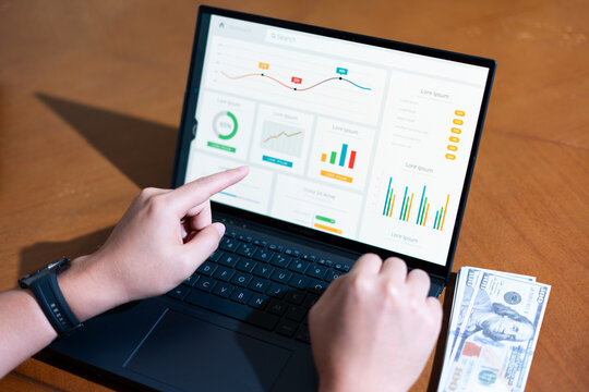 A person is pointing at a laptop screen with a graph on it