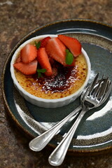 Fresh dessert served on a plate featuring classic crème brûlée topped with fresh strawberries.