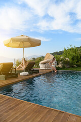 A brunette and blonde in their 20s relax together by their hotel room's private outdoor pool,...