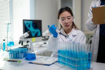 A woman in a lab coat is using a pipette to transfer liquid into a beaker