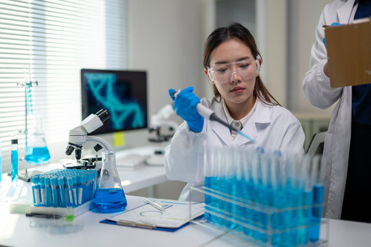 A woman in a lab coat is using a pipette to transfer liquid into a beaker