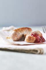 Grilled white sausage with ketchup on white paper tray. Rustic wooden background.
