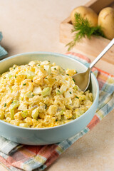 Vertical image of Potato salad made from boiled potatoes, boiled eggs, onions, celery, mustard, pickle, mayonnaise and paprika dressing.