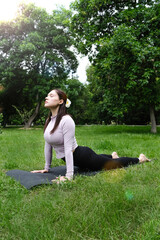 A woman is practicing yoga outdoors, surrounded by nature. She stands gracefully on a grassy field, focused and calm. 