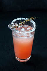 Salty Dog cocktail with fresh grapefruit juice, lime juice, and thyme, in a Collins glass with ice, on black