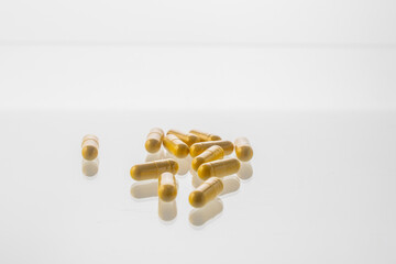 Yellow pills are scattered on a white background with a reflective surface.