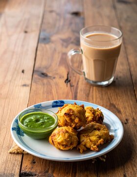 Traditional Indian pakoras with green chutney and masala chai tea on wooden table - authentic street food snacks and spiced tea for cultural cuisine