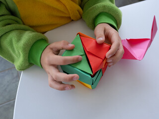 Kid opening a folded modular origami cube made of bright paper on white background.