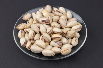 Heap of tasty pistachio nuts on the plate on dark background