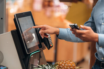 With pineapple. Close up view of man customer that is paying for products by credit card in grocery...