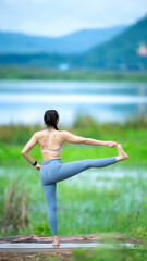 A woman is doing yoga on a grassy field. She is wearing a grey top and blue pants
