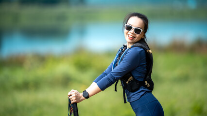 A woman wearing sunglasses and a blue shirt is standing in a grassy field. She is holding a tennis racket and a tennis ball