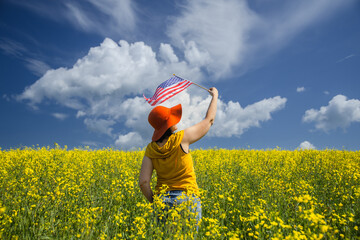 Woman with orange hat holding the American flag outdoors on a rapeseed yellow meadow.  4th of July...