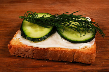Delicious canapés with cream cheese, cucumber and dill on wooden table