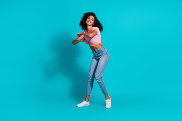 Young woman dancing joyfully in casual fashion with teal background