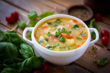 Homemade pea soup with vegetables and fresh basil in a white plate on a wooden table. Delicious pea soup for lunch. Close-up