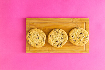 Three chocolate chip cookies on a wooden board