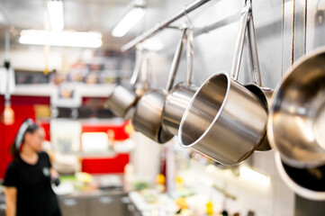 A professional kitchen featuring stainless steel pots hanging on a rack. The background showcases a...