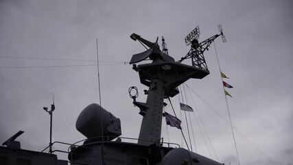 Silhouette of a Navy ship's radar and communication equipment rises into a cloudy sky representing maritime technology and defense systems for navigation and surveillance at sea