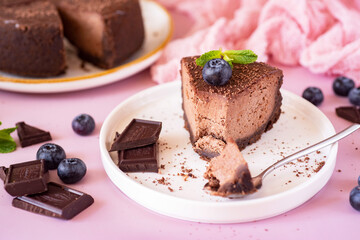 A piece of chocolate cheesecake on a white plate on a pink background. Chocolate cheesecake for dessert. Close-up