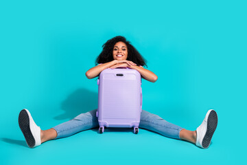 Joyful young woman smiling with a purple suitcase on a turquoise background showcasing cheerful...