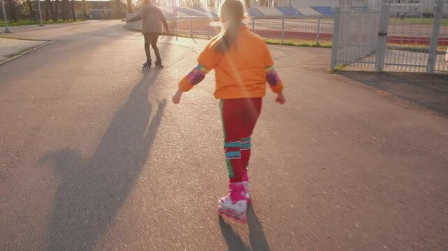 Low-angle view captures a child's vibrant rollerblading adventure on grey asphalt. Brightly colored clothing and pink skates symbolize youthful energy and freedom of movement.