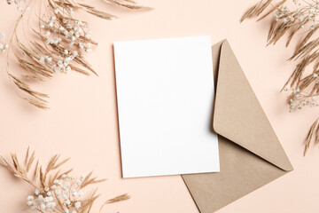 Vertical white blank card on beige background paired with kraft envelope, styled with dried grasses and baby breath, ideal for rustic wedding stationery mockups