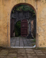 Open stone arch against the background of abandoned ancient buildings and antique ruins. In the background, broken door leaves. A mystical setting