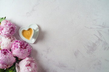 Heart shape coffee cup and peony flower bouquet on bright background. Feminine concept. Top view, flat lay