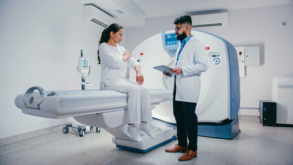 Charming woman sitting on medical bed gesturing toward wrist while explaining pain to male doctor....
