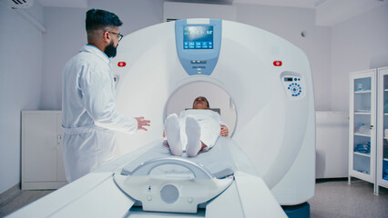 Bearded technician wearing lab coat turning control knob while medical bed carrying female patient...