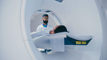 Caring technician watching closely as female patient lying on medical platform gradually sliding...